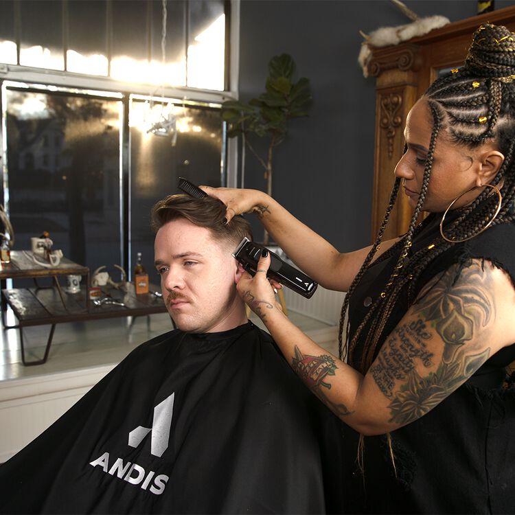 Barber using Andis black barber cape in barbershop